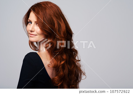 Terrific tresses. Studio shot of a young woman with beautiful red hair posing against a gray background. 107572922