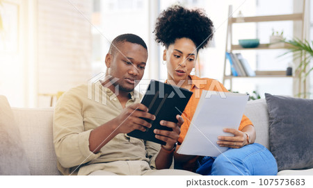 Black couple,tablet, documents and financial crisis on living room sofa discussing mortgage payment or loan at home. Frustrated African man and woman with paperwork in debt, finance issue or money pr 107573683