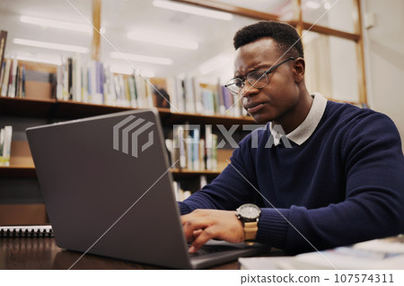Student, frustrated and black man typing on a laptop in university or college campus angry due to assignment project. Online, studying and young person prepare for internet exam or doing research 107574311