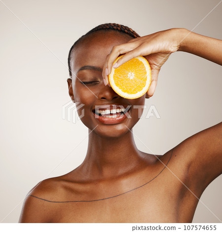 Black woman, orange fruits and beauty in studio for vitamin c, vegan cosmetics and facial on brown background. Happy model, citrus and nutrition for natural skincare, organic benefits and detox diet 107574655