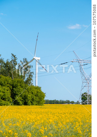 Wind turbine on grassy yellow field against cloudy blue sky in rural area during sunset. Offshore windmill park with stormy clouds in farmland Poland Europe. Wind power plant generating electricity 107575088