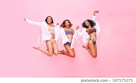 Jump, beauty and women friends in underwear in studio on a pink background for fun and skincare. Lingerie party, fitness and wellness of model group in air for diversity, body positive or inclusion 107575275