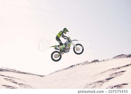 Bike, sand and jump with a sports man riding a vehicle in the desert for adventure or adrenaline. Motorcycle, training and ramp with an athlete outdoor in nature for freedom, power or competition Bike, sand and jump with a sports man riding a vehicle in the desert for adventure or adrenaline. Motorcycle, training and ramp with an athlete outdoor in nature for freedom, power or competition 107575435