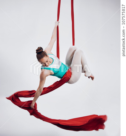Gymnastics, aerial acrobat and sports with a woman in air for performance and balance. Young athlete person or gymnast hanging on red silk fabric and white background with space, art and creativity 107575817