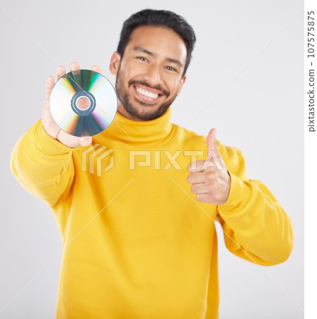 Man, portrait and CD with thumbs up and happy from music of DVD in studio. Smile, motivation and like emoji hand sign of a male person with white background and holding multimedia disk of audio 107575875