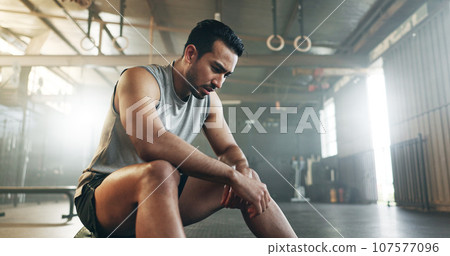 Fitness, breathing and sweating with a tired man in the gym, resting after an intense workout. Exercise, health and fatigue with a young athlete in recovery from training for sports or wellness 107577096