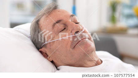 Oxygen, hospital bed and senior man sleeping with ventilation and breathing tube support in a clinic. Elderly patient, medical care and emergency room with male person at a doctor for healthcare Oxygen, hospital bed and senior man sleeping with ventilation and breathing tube support in a clinic. Elderly patient, medical care and emergency room with male person at a doctor for healthcare 107577554