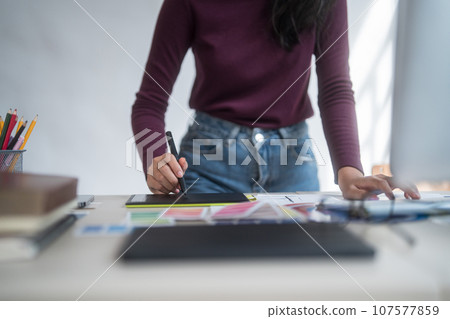 Graphic designer freelance women writing on digital tablet to thinking creative ideas for logo brand while typing on computer and working about graphic design with technology equipment in home studio 107577859