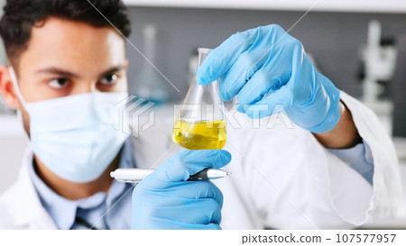 A thinking young scientist doing research to create a covid cure in a lab. Medical professional using science equipment in a laboratory. A serious male healthcare worker working with a mask. 107577957