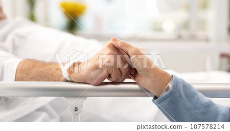 Hospital bed, support and senior couple holding hands, trust or comfort sick partner with healthcare problem. Bedroom, marriage love or elderly people care for mental health patient with medical risk 107578214
