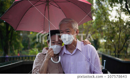 Asian senior elder couple walking in raining park share umbrella fun romantic love lifestyle Asian senior elder couple walking in raining park share umbrella fun romantic love lifestyle 107578643