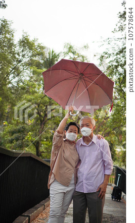 Asian senior elder couple walking in raining park share umbrella fun romantic love lifestyle Asian senior elder couple walking in raining park share umbrella fun romantic love lifestyle 107578644