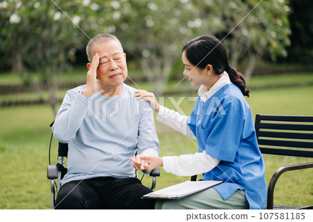 Elderly asian senior man on wheelchair with Asian careful caregiver. Nursing home hospital garden concept. 107581185