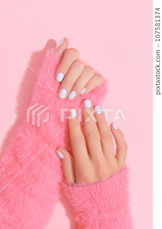 Womans hands with white nail design on pink background 107581374