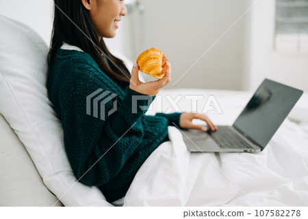 Beautiful young asian woman on a white bed with coffee cub and using smart phone at home. lifestyle concept 107582278