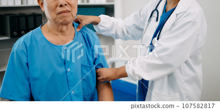 Asian physiotherapist helping elderly man patient stretching arm during exercise correct with dumbbell in hand during training hand in bed in clinic Asian physiotherapist helping elderly man patient stretching arm during exercise correct with dumbbell in hand during training hand in bed in clinic 107582817