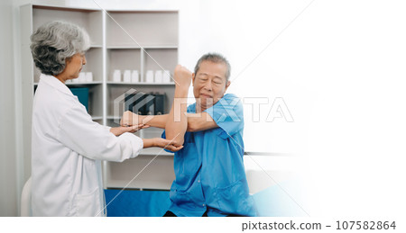 Asian physiotherapist helping elderly man patient stretching arm during exercise correct with dumbbell in hand during training hand in bed in clinic 107582864