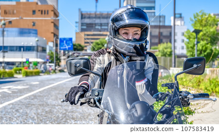 A smiling female rider touring Yokohama on a large American motorcycle A smiling female rider touring Yokohama on a large American motorcycle 107583419