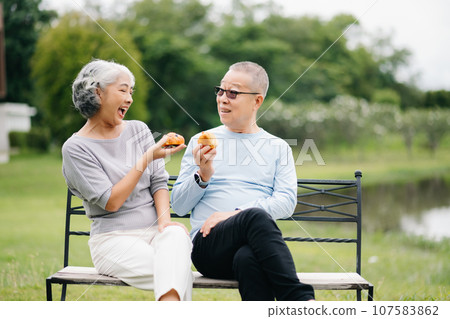 Asian senior couple having a good time. They laughing and smiling while sitting outdoor at the park. Lovely senior couple. 107583862