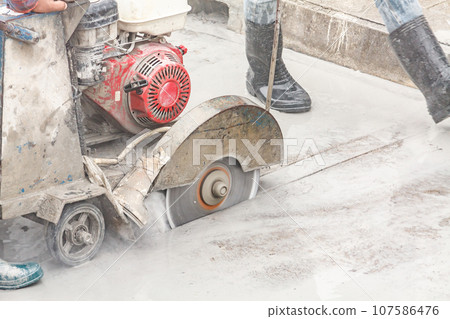 Worker using diamond saw blade machine cutting concrete road at construction site Worker using diamond saw blade machine cutting concrete road at construction site 107586476