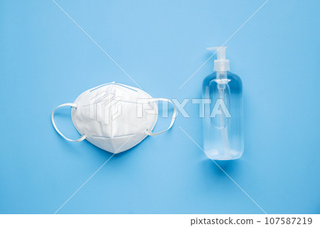 Alcohol hand sanitizer gel bottle with KN95 surgical face mask on blue background protection against COVID-19 coronavirus. Healthcare and medical concept Alcohol hand sanitizer gel bottle with KN95 surgical face mask on blue background protection against COVID-19 coronavirus. Healthcare and medical concept 107587219