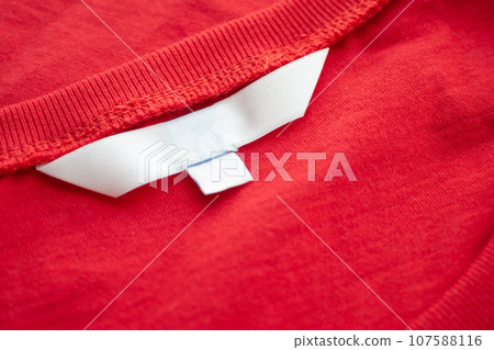 White blank clothing tag label on new red cotton shirt fabric texture background 107588116
