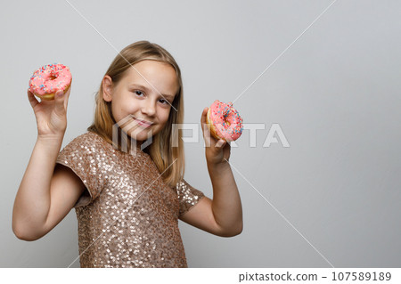 Cute smiling child girl with tasty pink donut on gray background. Holiday birthday party concept 107589189