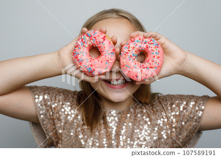 Portrait of happy young girl with colorful pink donut on gray background. Portrait of happy young girl with colorful pink donut on gray background. 107589191