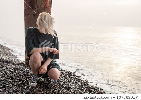 Casual young woman with blonde hair sitting on sea beach Casual young woman with blonde hair sitting on sea beach 107589317