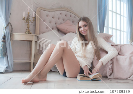 Happy cheerful young blonde woman reading a book and resting in bedroom at home Happy cheerful young blonde woman reading a book and resting in bedroom at home 107589389