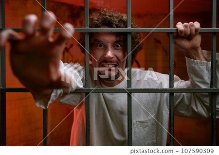 Angry crazy man prisoner and psychiatric hospital patient in cage 107590309