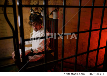 Mad man screaming feeling madness on electric chair at psychiatric hospital 107590311