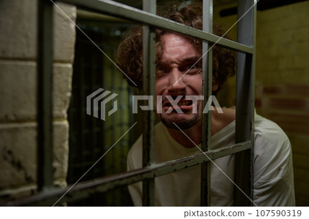Portrait of crazy man with mad face crying bitterly in cage 107590319