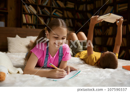 Little sister and brother doing homework lying in bed 107590337