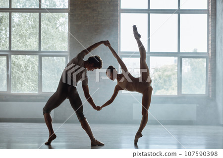 Silhouette of man and woman ballet dancers performing together against studio background 107590398
