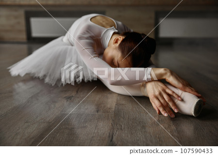 Young graceful ballerina dressed tutu posing on floor while training in studio 107590433