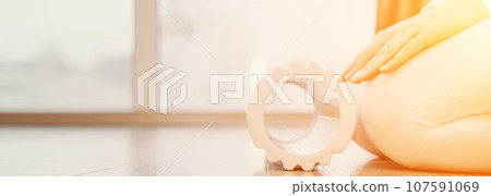 Adult athletic woman, in white bodysuit, performing fascia exercises on the floor - caucasian woman using a massage foam roller - a tool to relieve tension in the back and relieve muscle pain - the 107591069