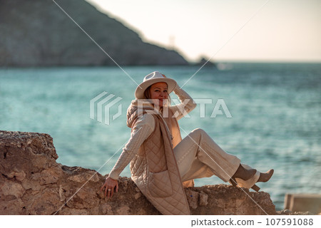 Happy blonde woman in a white suit and hat posing at the camera against the backdrop of the sea 107591088