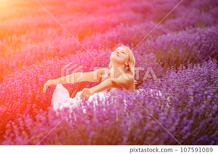 Woman lavender field. A middle-aged woman sits in a lavender field and enjoys aromatherapy. Aromatherapy concept, lavender oil, photo session in lavender 107591089