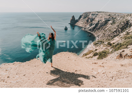 Woman green dress sea. Female dancer posing on a rocky outcrop high above the sea. Girl on the nature on blue sky background. Fashion photo. Woman green dress sea. Female dancer posing on a rocky outcrop high above the sea. Girl on the nature on blue sky background. Fashion photo. 107591101
