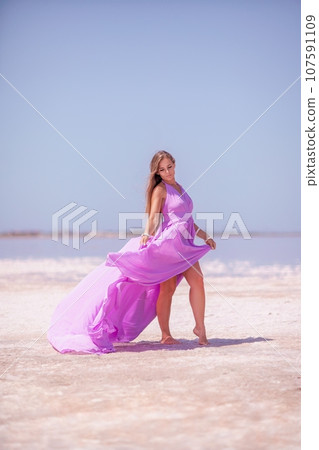 Woman pink salt lake. Against the backdrop of a pink salt lake, a woman in a long pink dress takes a leisurely stroll along the white, salty shore, capturing a wanderlust moment. Woman pink salt lake. Against the backdrop of a pink salt lake, a woman in a long pink dress takes a leisurely stroll along the white, salty shore, capturing a wanderlust moment. 107591109