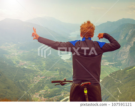Boy sit on mountain bike and watching from Alps peak 107591121