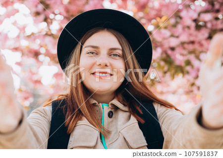 Young happy woman wearing hat taking selfie on spring city street. 30s girl smiling enjoying spring summer day. High quality photo 107591837