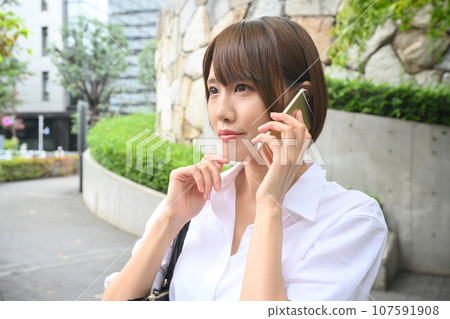 A woman calling on a smartphone on the side of a sidewalk in the city 107591908