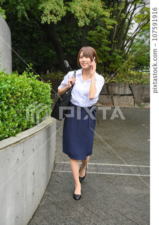 一位女士在城市的人行道上行走時打電話給她的智慧型手機 107591916