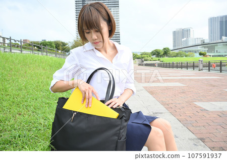 女人坐在戶外,看著包包裡的東西 女人坐在戶外,看著包包裡的東西 107591937