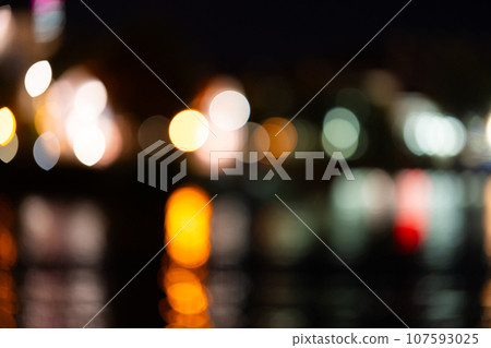 Blurred background of a night city and a body of water. Bright glowing lights of an area in a metropolis under a twilight sky in the evening on a blurred background 107593025