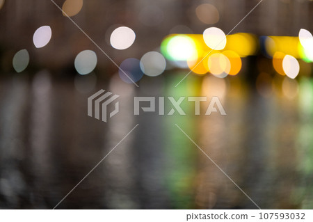 Blurred background of a night city and a body of water. Bright glowing lights of an area in a metropolis under a twilight sky in the evening on a blurred background 107593032
