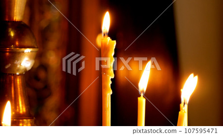 A woman's hand puts a burning candle near an orthodox cross in a church. Church Prayer Concept 107595471
