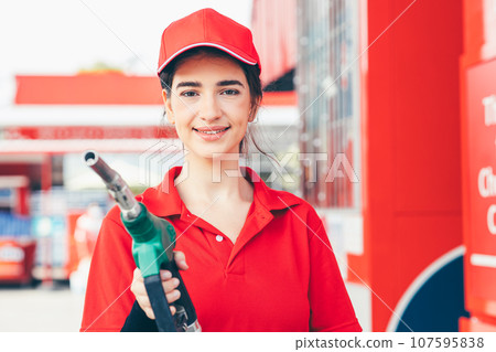 Gas station service staff worker women happy smiling with fuel nozzle for car gasoline refill job Gas station service staff worker women happy smiling with fuel nozzle for car gasoline refill job 107595838